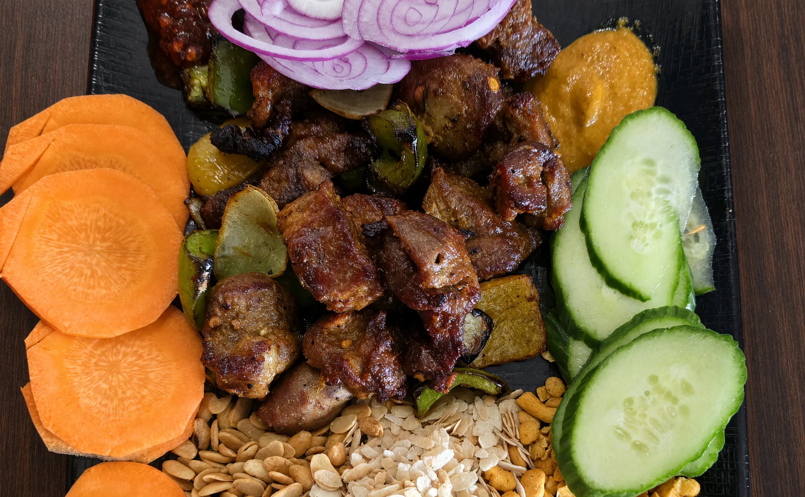 Grilled meat with red onion, carrot, cucumber and beaten rice on a Nepali platter