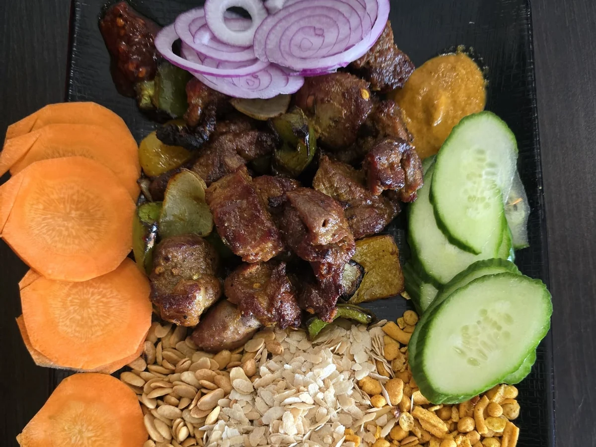 Nepali platter of grilled meat with beaten rice, peanuts, carrot, cucumber and achar